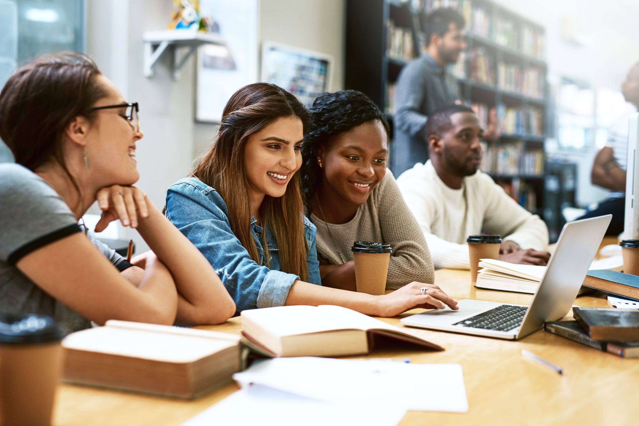 a group of students working on assignments in the library using a laptop